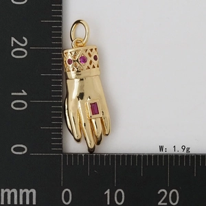 Vue détaillée du pendentif main en or avec pierre rouge sur une règle de mesure précise
