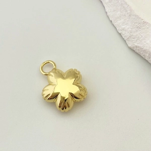 Close-up of a polished gold flower pendant with textured petals and a top ring loop
