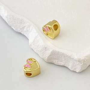 Dettaglio di ciondoli a cuore dorati con fiocco in smalto rosa a pois per la creazione di gioielli