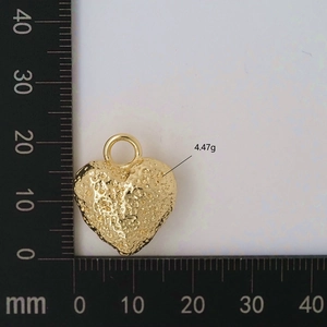 Macro shot of 20mm heart-shaped golden pendant with hammered metal texture on ruler