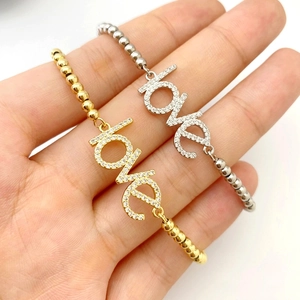 Macro detail of gold and silver beaded bracelets with sparkling love charm in palm