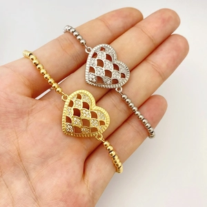 Close-up of heart-shaped hollow charms with inlaid crystals on gold and silver beaded bracelets