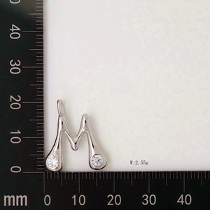 Detail showing letter M pendant with cubic zirconia and a ruler for measurement
