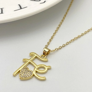 Dettaglio del ciondolo con lettera Fé dorata con cuore e zirconi micro-pavé