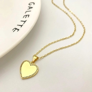 Dettaglio di una collana con ciondolo a cuore dorato con bordo perlato su vassoio bianco