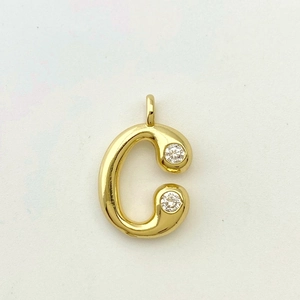 Macro detail of gold letter C pendant with sparkling cubic zirconia on polished finish