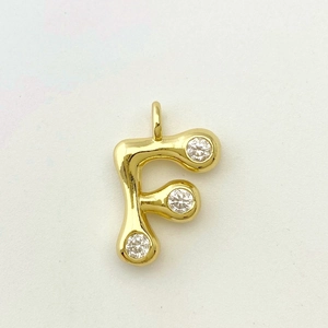 Detailed close-up of a golden letter F pendant with three sparkling zircon stones
