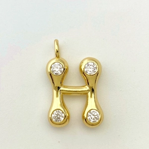 Close-up of golden letter H pendant with four sparkling zircons on textured background