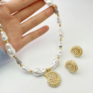 Close-up of baroque pearl necklace and golden shell earrings set held by a hand