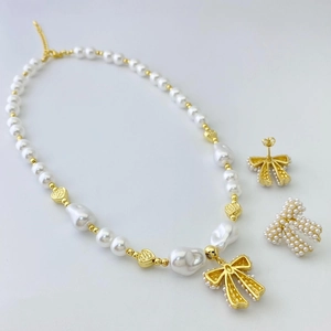 Close-up of pearl bow necklace and earrings set with gold heart charms and baroque pearls