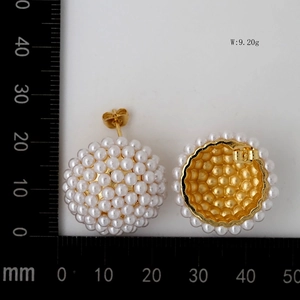 Detail of white dome pearl earrings with gold base next to a size measuring scale