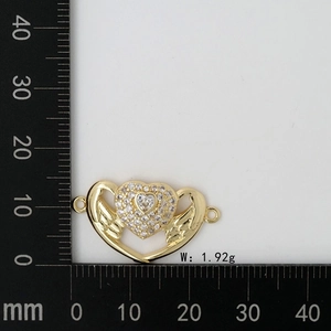 Golden heart-shaped charm with angel wings and zircons measured on a black scale