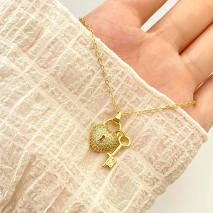Macro detail of a gold heart-shaped lock and key pendant necklace with zircon stones