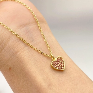 Collana a cuore dorata con micro-pavé di zirconi rossi su una sottile catena a incrocio