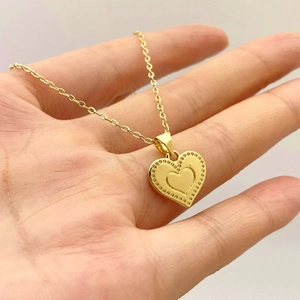 Detail view of heart-shaped gold pendant with milgrain edge held in hand for size