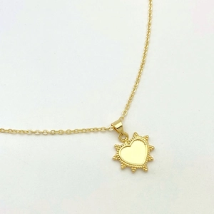 Detail of a golden heart pendant with a radiant beaded edge on a delicate thin chain