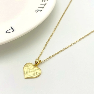 Detail of a golden heart pendant necklace with dotted texture and a fine O-link chain