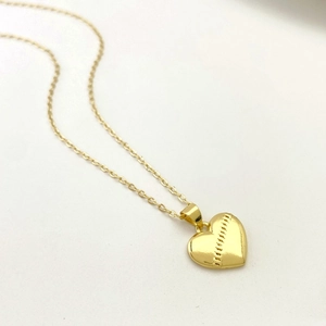 Macro shot of gold heart pendant with baseball stitching texture on thin O-chain