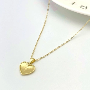 Macro detail of a golden heart pendant necklace with refined hammered texture on white