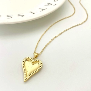 Detailed macro view of a gold heart pendant with vintage textures and a fine cross chain