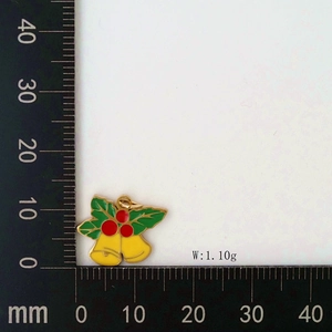 Detailed view of enamel Christmas bell pendant with green leaves shown on a metric scale