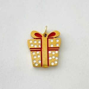Macro detail of a golden gift box charm with red enamel ribbons and white polka dots