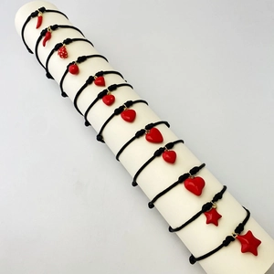 Close-up of handmade black woven bracelets with red heart and chili charms on a stand