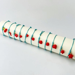 Handmade sky blue woven bracelets with red heart and cherry charms on white display stand