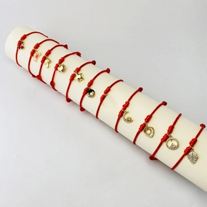 Macro detail of red woven bracelets with gold charms like heart moon and leaf shapes