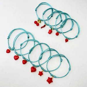 Close-up of turquoise woven cord bracelets with red heart and cherry charms