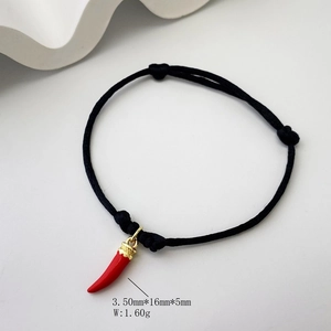 Macro shot of black braided rope bracelet with red chili charm and gold metal detail