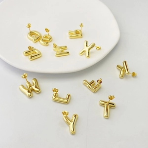 Puffy golden alphabet stud earrings in 3D balloon style for women on white ceramic plate