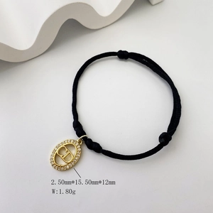 Detail of black woven cord bracelet with gold oval CD pendant and sparkling zircons