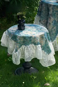 Detail of blue floral jacquard tablecloth with wide white lace ruffled edges in a garden