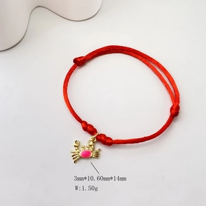 Detail of red braided bracelet featuring a golden crab charm with pink enamel inlay