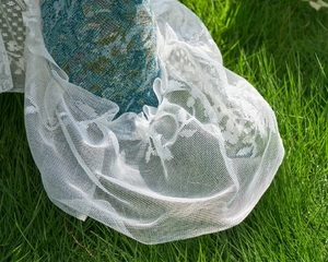Close-up of white lace ruffle border on blue Monet jacquard fabric over green lawn