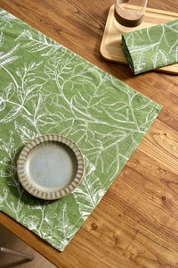 Detail of green table runner with white leaf prints on a natural wooden dining table