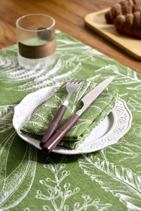 Detail of green maple leaf print linen napkin and runner with rustic wooden tableware