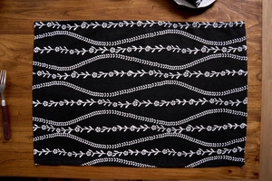 Detail of Nordic style black floral cloth placemat on a rustic wooden dining table surface
