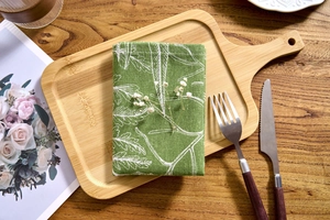 Detail of green cotton linen napkin with white leaf print on a bamboo tray set on wooden table
