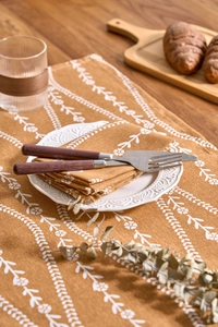 Detail of floral printed napkins with wood handle cutlery and white ceramic plate