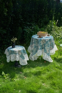 Classic blue floral tablecloth with elegant white lace ruffle edges in a garden setting