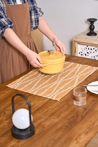 Hands placing a yellow round enamel cast iron dutch oven on a wooden dining table