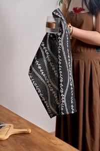 Close-up of black floral linen napkin being used to dry a glass cup in a kitchen setting