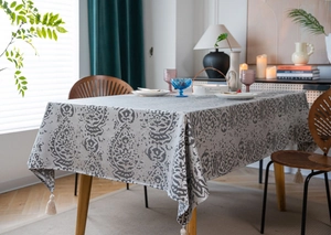 Detail of grey paisley table cloth with white corner tassels on a wooden dining table