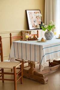 Detailed view of white cotton-linen tablecloth featuring blue embroidery and fringe edges
