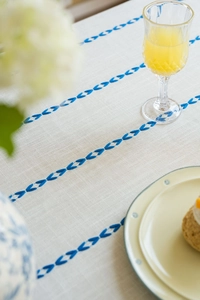Close-up of beige linen tablecloth featuring blue embroidered leaf patterns and fabric texture