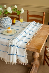 Close-up of blue geometric embroidery and beige fringe on a rustic linen tablecloth