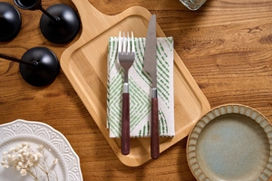 Close-up of rustic wooden tray with stainless steel cutlery and green leaf cloth napkin