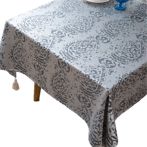 Nordic grey jacquard tablecloth with damask pattern and white tassels on a wooden table